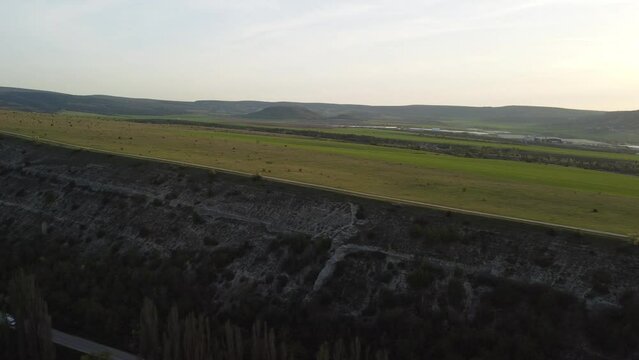 AERIAL: Flying over a small herd of cattle cows walking uniformly down farm road on the hill. Black, brown and spotted cows. Top down view of the countryside on a sping sunset. Idyllic rural landscape