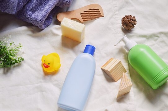 Flat lay photo baby care bath products, natural cosmetics. Blue shampoo bottle, green liquid soap package, yellow rubber duck, wooden comb, purple towel still life photography