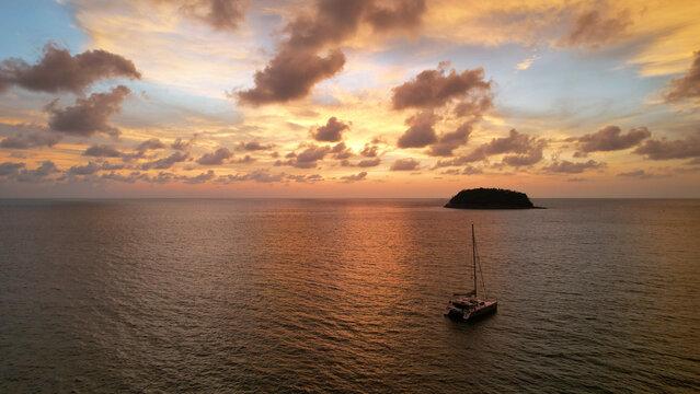 Luxury Yacht At An Epic Sunset With A View Of The Island And Incredible Orange Clouds. The Sky Is Reflected In The Water. A Lonely Island In The Distance. Calm. Top View From Drone. Kata Beach Phuket