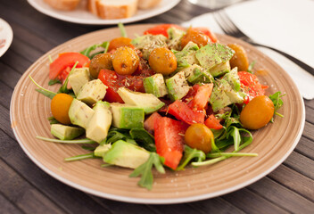 fresh salad of arugula, avocado, cherry tomatoes with olives on brown plate