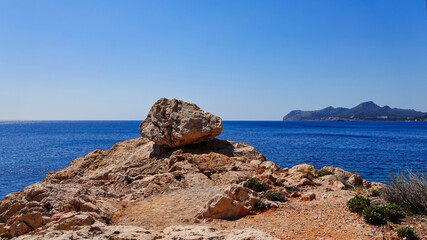 Fototapeta na wymiar Ein Felsbrocken vor offener Meereskulisse, mit strahlend blauem Himmel und einer Landzunge im Hintergrund