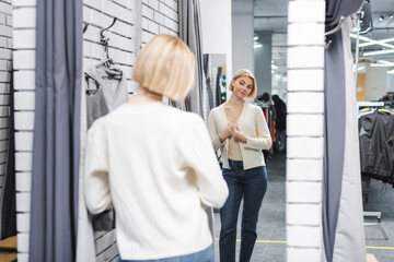 Blurred woman looking at mirror in dressing room in second hand.