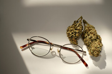 Ophthalmology and cannabis concept. Marijuana buds with glasses on white background. Alternative...