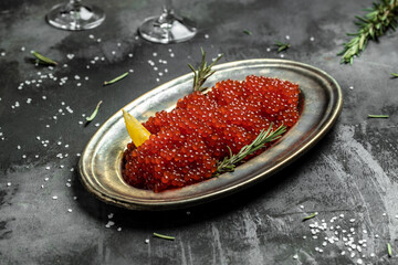Red caviar filling metal plate and a glass of champagne on a stone background. Gourmet food close up, appetizer, selective focus, place for text