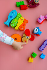 Child is playing with colorful wooden and plastic toys, on pink background