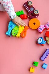 Fototapeta na wymiar Child is playing with colorful wooden and plastic toys, on pink background