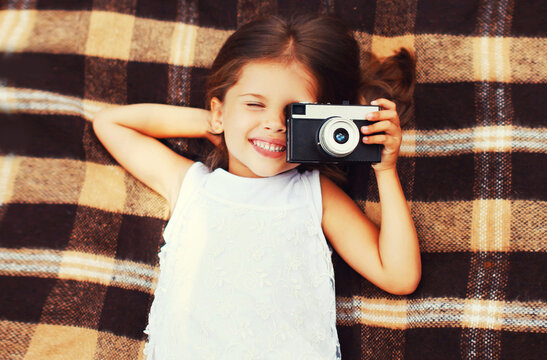 Summer portrait of happy smiling little girl child with film camera taking picture lying on plaid background