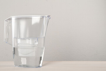 Filter jug with purified water on white table against light background. Space for text