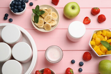 Modern yogurt maker with full jars and different fruits on pink wooden table, flat lay