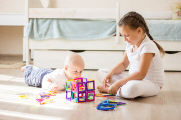 Cute children infant boy and little girl playing with toy magnetic construction set at home.