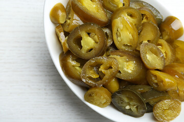 Bowl with slices of pickled green jalapeno peppers on white wooden table, top view
