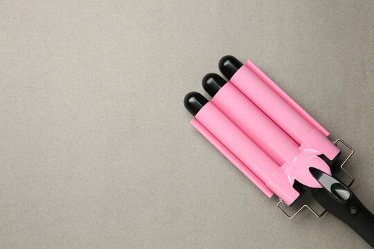 Modern triple curling hair iron on grey background, top view. Space for text
