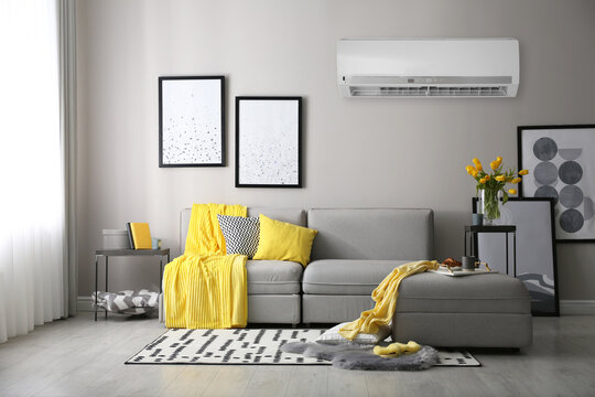 Modern air conditioner on light grey wall in living room with stylish sofa