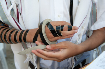 Close-up view of a bar mitzvah boy wrapping the leather straps of his tefillin or phylacteries...