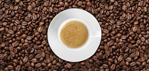 Fototapeta premium Cup of tasty aromatic coffee on roasted beans, top view. Banner design