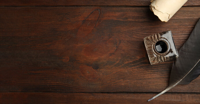 Quill, inkwell and parchment scroll on wooden table, flat lay with space for text. Banner design