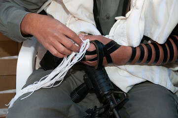 An Israeli soldier police officer holds the tzitzit strings on his tallit while reciting the...