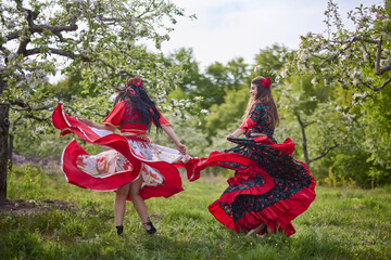 two dancers in traditional gypsy dresses dance in nature on a spring day