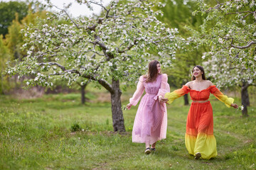 Beautiful women enjoying the garden with flowering trees, young women with flowers in the green park. cheerful teenagers walking outdoors. soft light style color