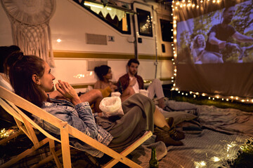 Young cheerful people watching a movie on camping site - obrazy, fototapety, plakaty