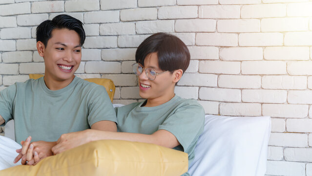 Happy gay asian couple lying on a bed together and smile.