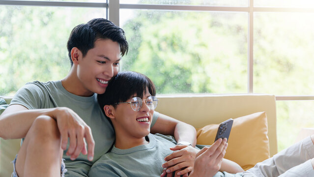 Gay asian couple looking at smartphone together indoors.