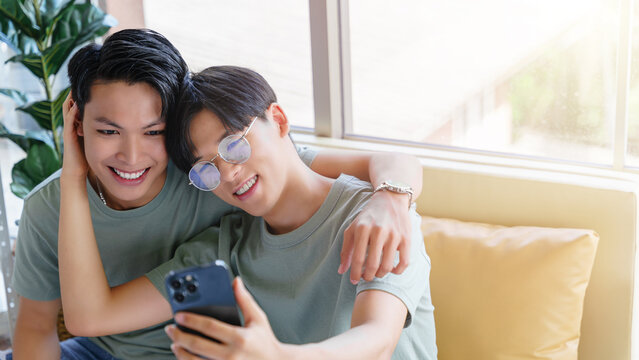 Happy gay asian couple taking a photo with smartphone. 