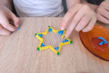 close-up of children's hands creating perler bead patterns, make crafts using thermomosaic...