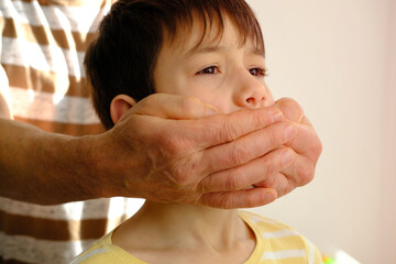 closeup rude male hands cover the mouth of a child, a boy suffers from violence, concept of parenting, punishment for bad words, children's jokes, teasing, ban on his opinion - obrazy, fototapety, plakaty