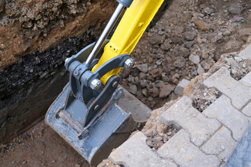 excavator bucket digs earth in trench on street, concept of repairing urban communications,...