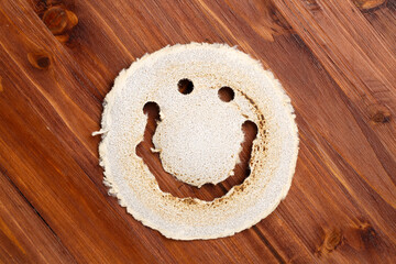 Top down view of an used, round sandpaper disk, looking like a smiling face, on a dark wood surface