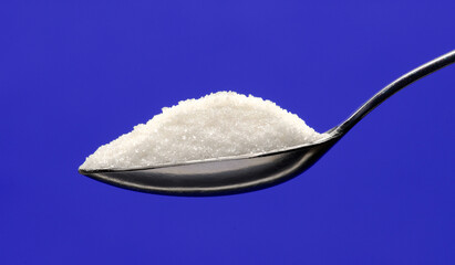 White sugar teaspoon on blue background.