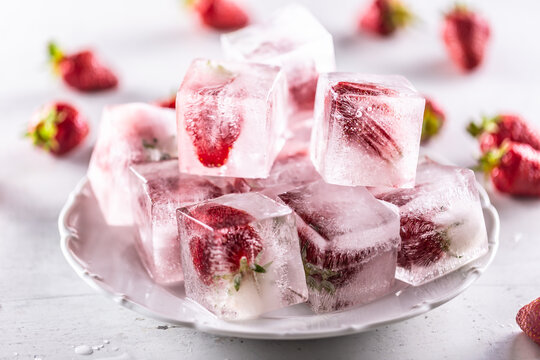 Frozen strawberries in ice cubes on a plate.