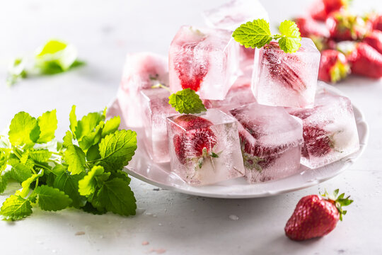 Frozen strawberries in ice cubes on a plate.