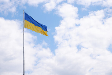 Flag of Ukraine on a high flagpole isolated on a blue sky background.