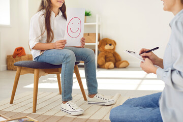 Kid who's learning to express positive emotions is showing happy emoticon card at interview...