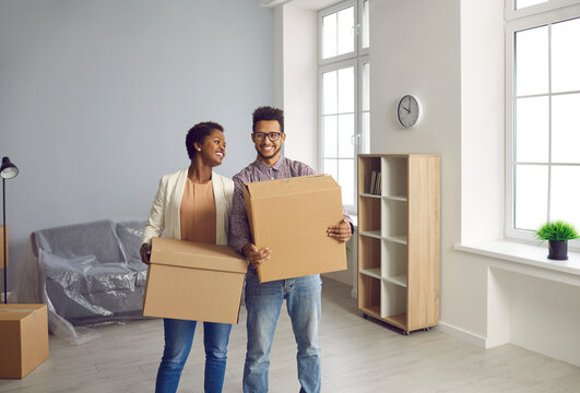 Happy black married couple settling down at new place and carrying big boxes together. Two young people who took out residential mortgage for house or apartment of their dream are moving into new home