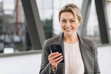 Fototapeta premium Portrait of a beautiful mature business woman in suit and gray jacket smiling and talking on the phone on the modern urban background