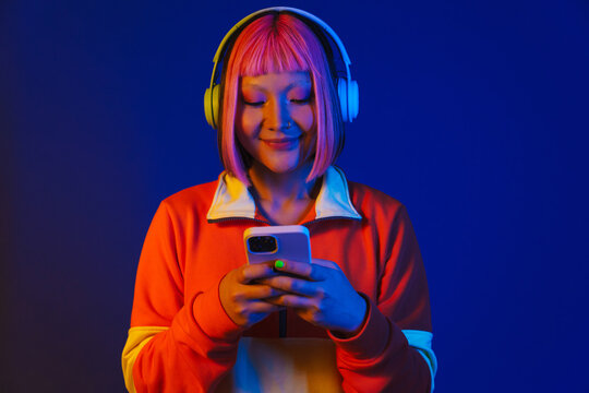 Asian girl in headphones smiling and using mobile phone