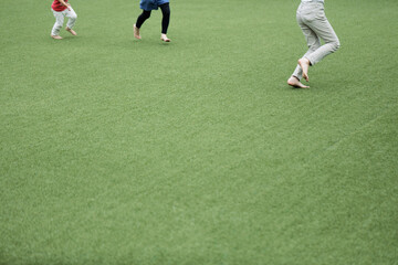 Fototapeta premium Legs of happy kids running in green field. Space for copy.