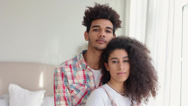 4k Young couple in love is hugging and posing with positive emotions in home room spbi. Close view of caucasian curly woman, man look ahead and pose with happy smiles, hug tenderly and stand in light