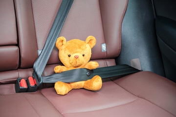 Yellow bear doll fastening seat belt during sitting inside a car and driving on the road. Car Seat, safety, trip, journey and transport concept