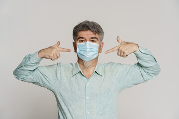 Mature man wearing shirt pointing fingers at his face mask