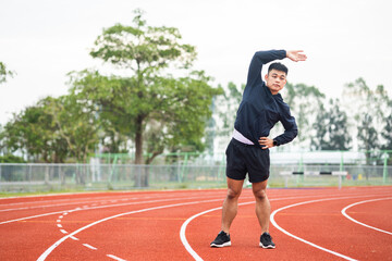 Fototapeta premium Young asian man wearing sportswear warming up front of sport stadium. Chinese man stretching arms before running on track exercise in the morning. Healthy and athlete lifestyle concept.