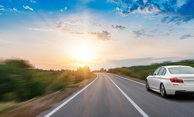 A white car drives along a beautiful road on a sunny summer day.
