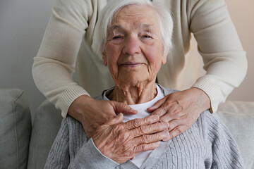 Unrecognizable female expressing care towards an elderly lady, hugging her from behind holding...