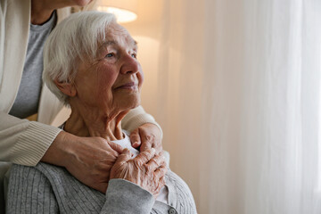 Unrecognizable female expressing care towards an elderly lady, hugging her from behind holding...