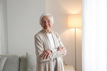 Portrait of elderly lady in beige cardigan alone at home. Senior woman 86 years of age standing by...