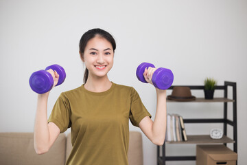 Attractive asian young fitness woman lifting dumbbell weights workout at home in living room. Fresh feeling female training and exercise wearing sport wear fit body.