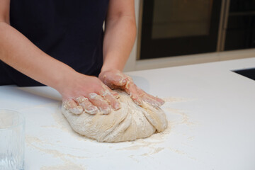 Obraz na płótnie Canvas Home cooking. A young woman works with yeast dough in a modern kitchen. A young woman is kneading a dough, engaged in cooking homemade bakery.